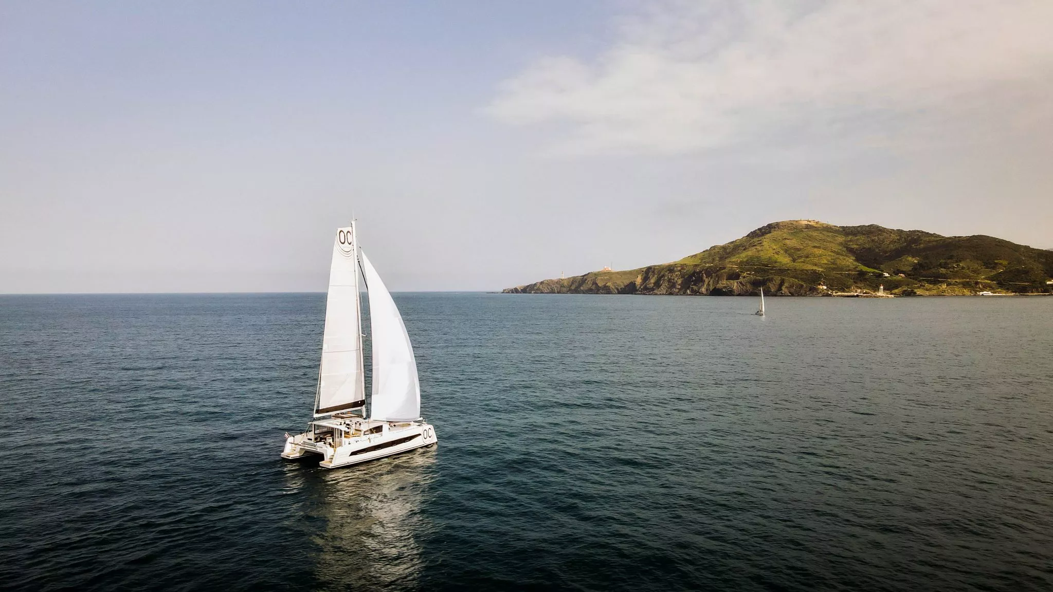 Catana catamaran sailing on open water with coastline in the background