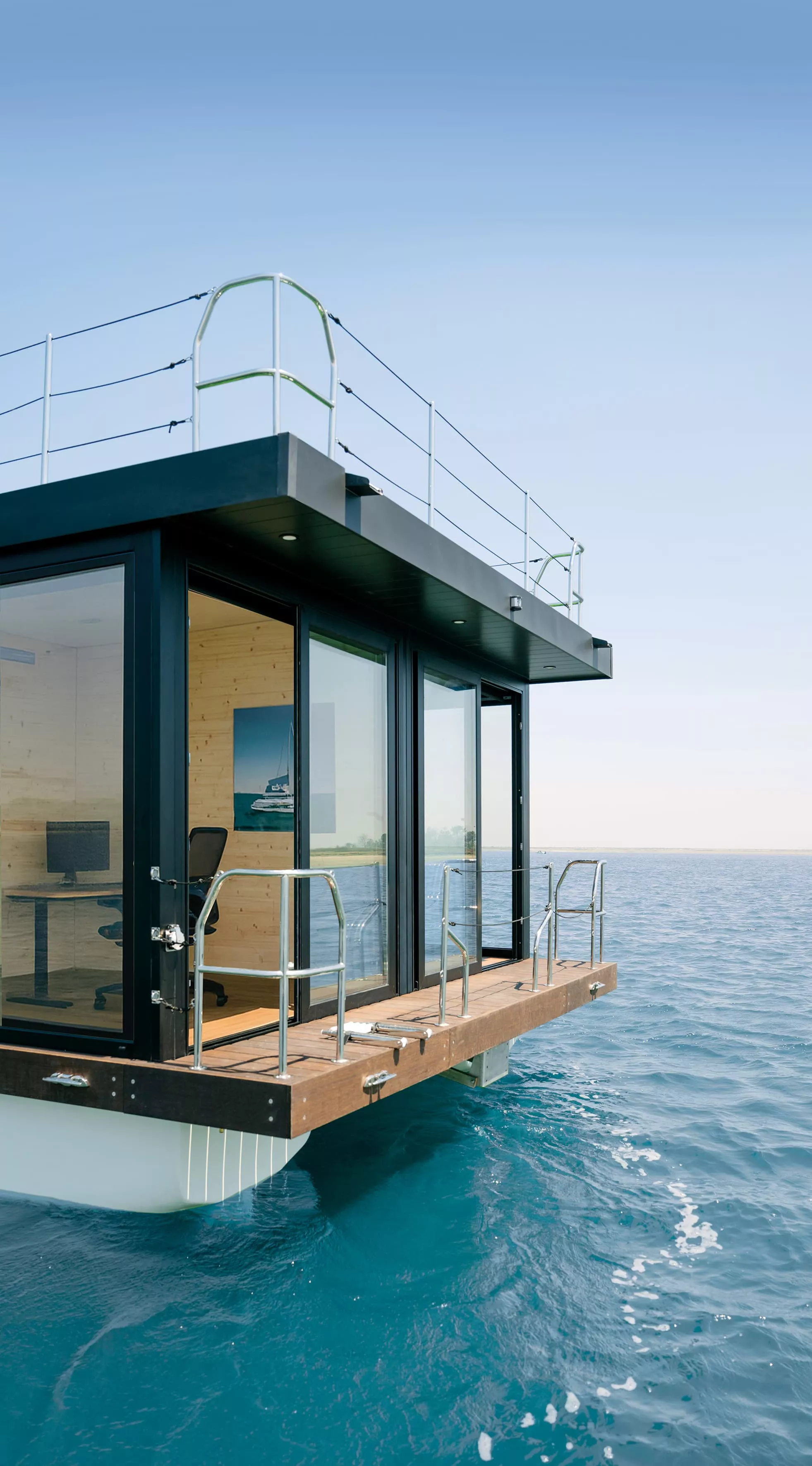 Corner exterior view of a floating office with glass walls and wooden deck on open water