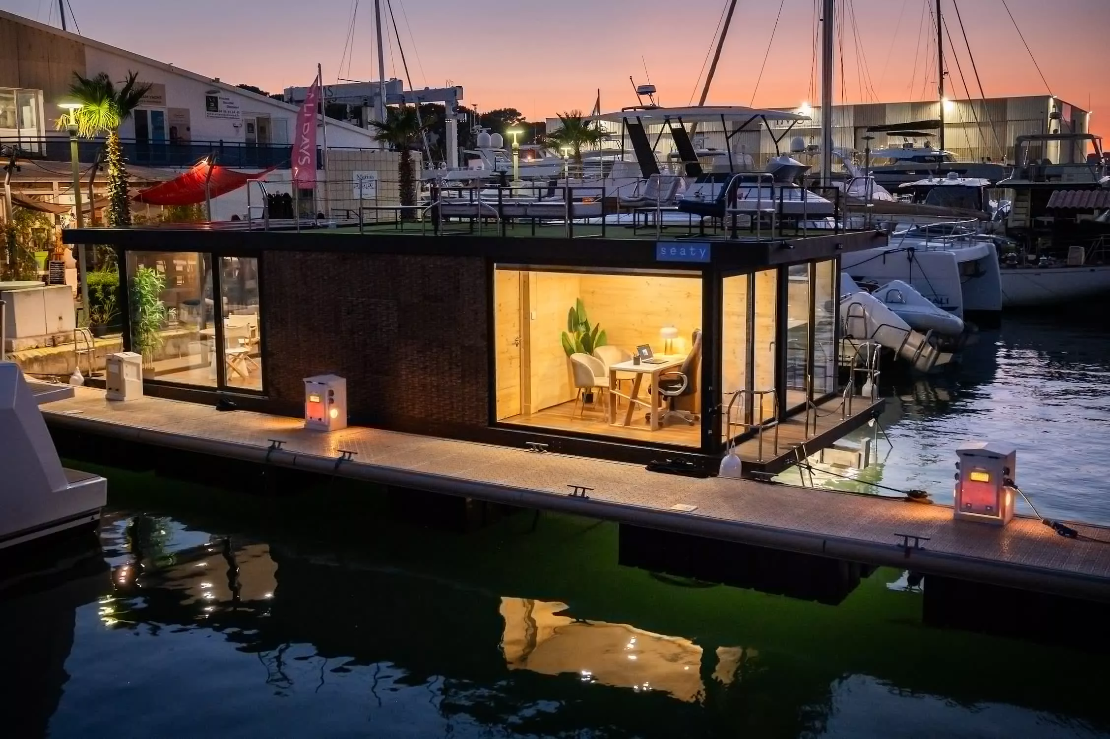 Floating office platform illuminated at sunset in a marina, with glass windows and interior workspace visible