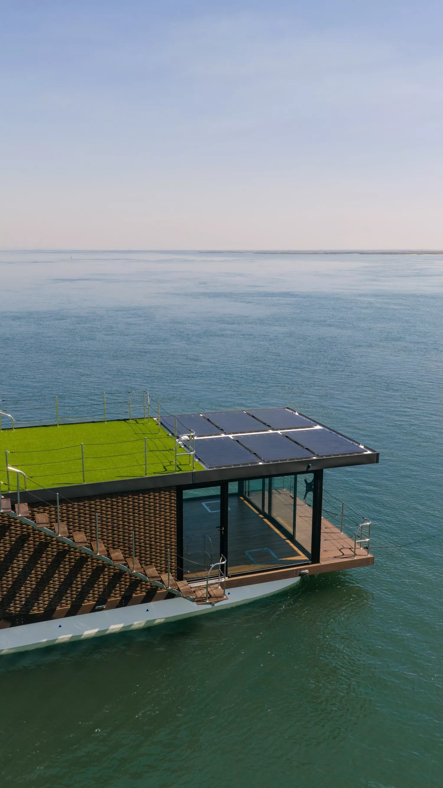 Floating platform with rooftop access and solar panels on open water under clear sky