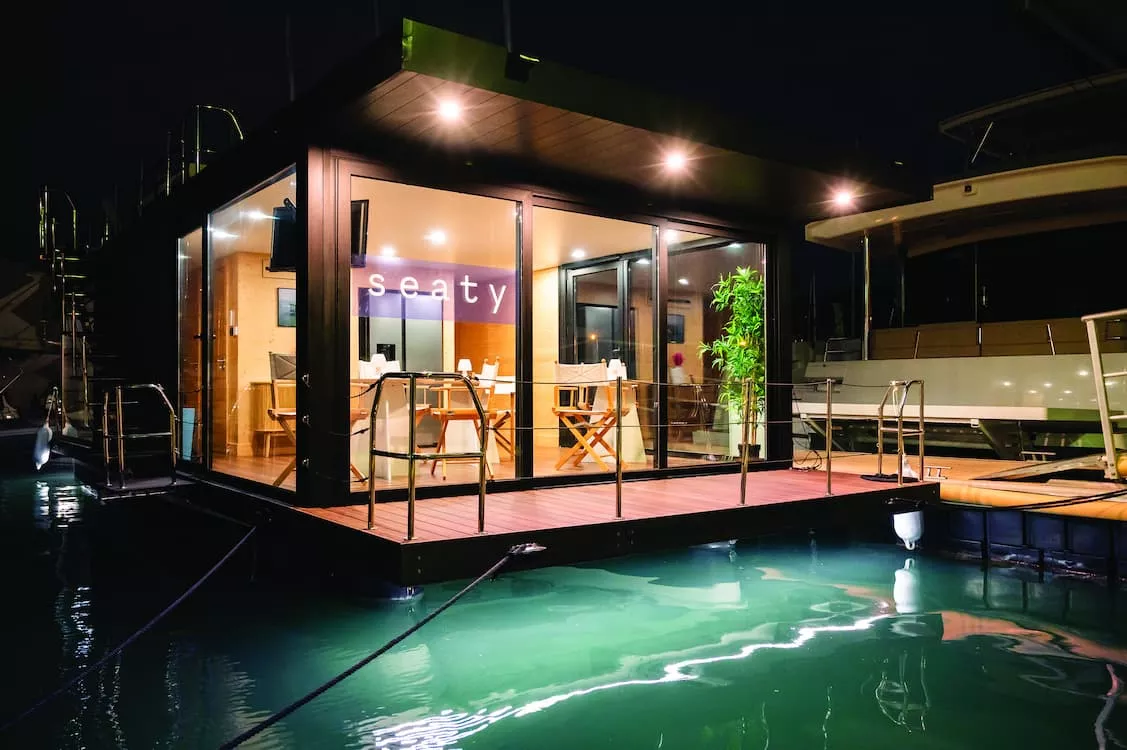 Floating office platform at night with large glass windows, wooden deck and soft interior lighting